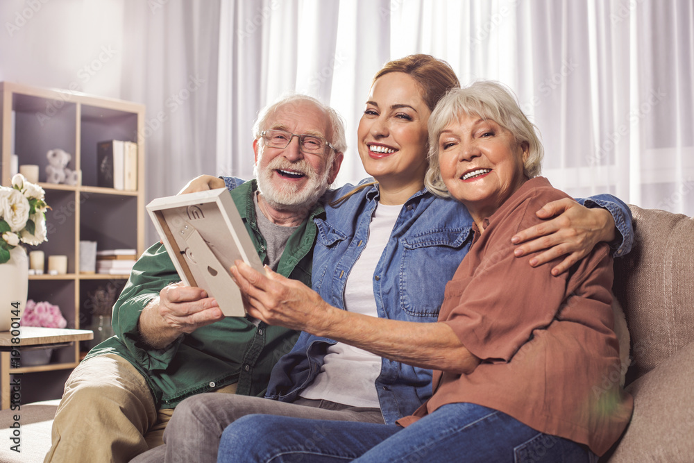 Φωτογραφία Portrait of cheerful bearded grandpa, cheerful daughter and beaming wife holding frame