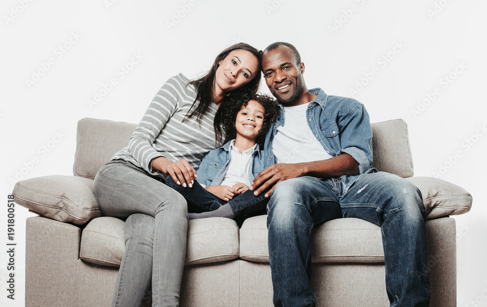 Portrait of happy young family sitting together on divan and looking at camera. Isolated on background