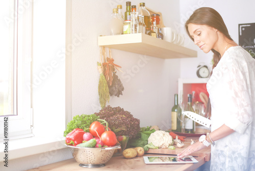 Young woman using a tablet computer to cook in her kitchen . Young woman