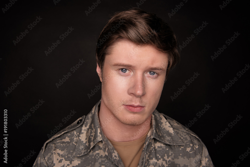 Cheerless young veteran looking at camera with upset look. He is feeling hopeless and loneliness. Isolated on black background