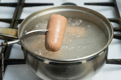 To get out of a pot of boiling water boiled sausages. The hot sausage is on the fork. Cooking at home on the gas stove.