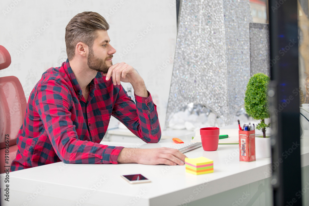 Concentrated on work. Concentrated young beard man working on laptop while sitting at his working place in office Concentrated on work. Concentrated young beard man working on laptop while sitting at his working place in office