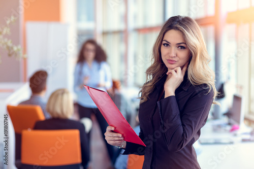 Business woman with folders standing and team mates working in meeting room at office.