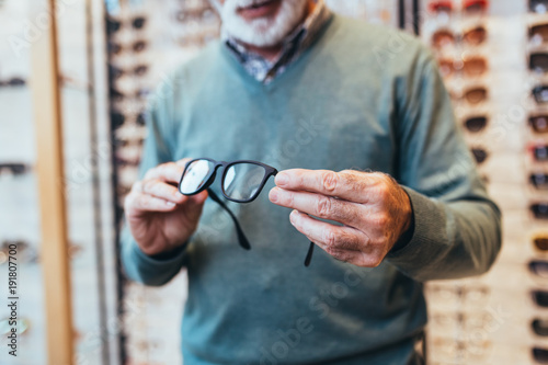 Photos Handsome senior man choosing eyeglasses frame in optical store.