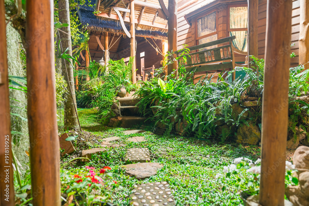 Stepping stones through lush deep green tropical garden and structure of rustic cottage.