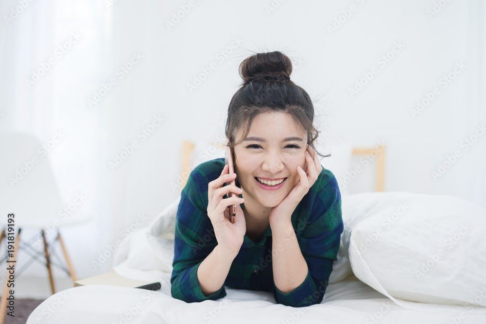 A woman using her smartphone as she lies down the length of the bed. A woman using her smartphone as she lies down the length of the bed.
