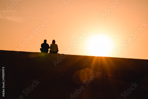 Paar sitzt auf der Düne in der Wüste und schaut in den Sonnenuntergang