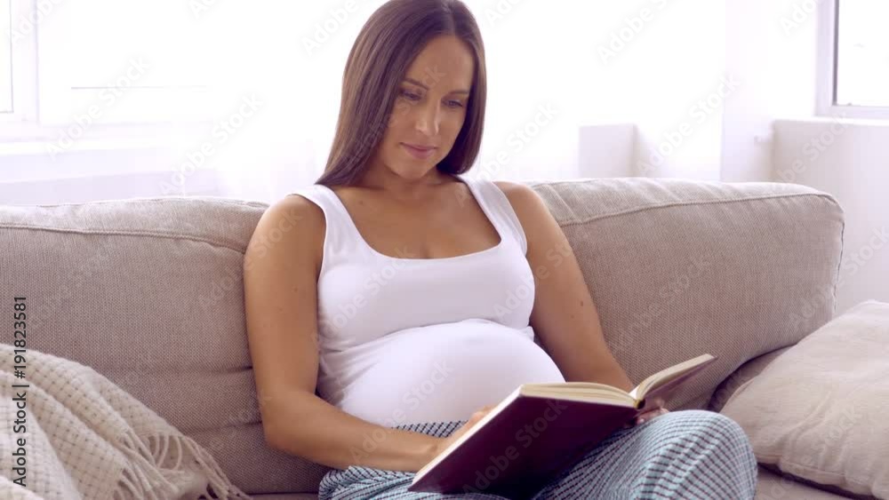 Affectionate future mother reading book on sofa Affectionate future mother reading book on sofa