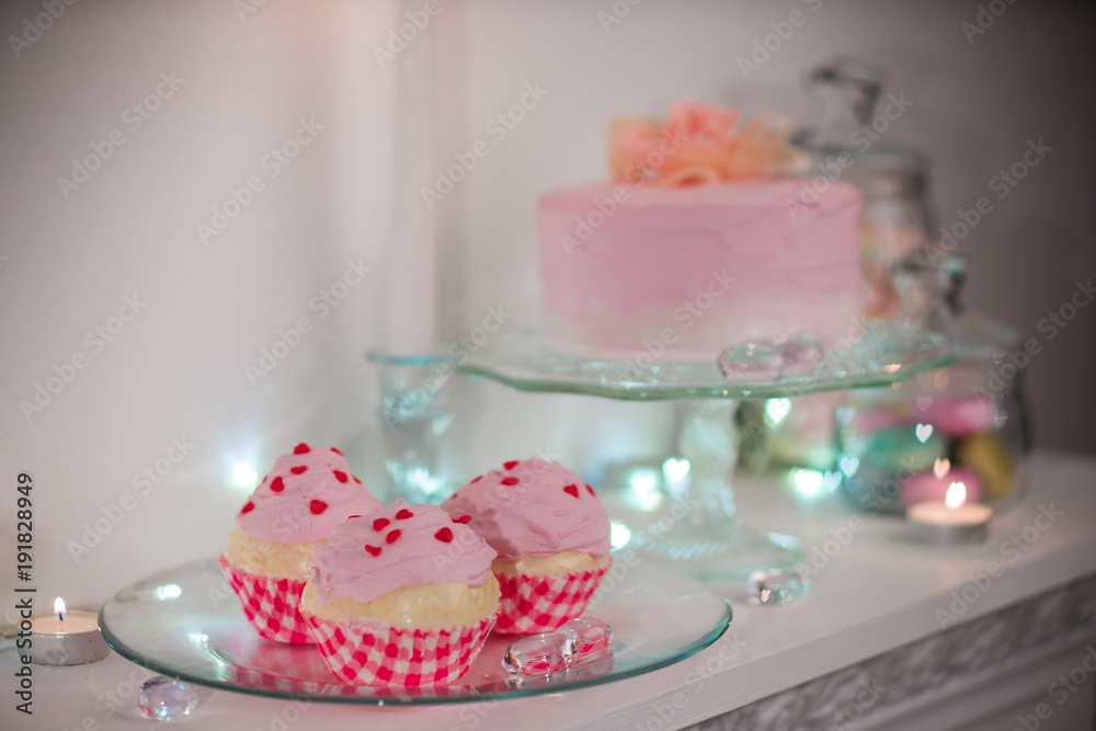 pink cake with mastic on white table surrounded by colorful sweets pink cake with mastic on white table surrounded by colorful sweets