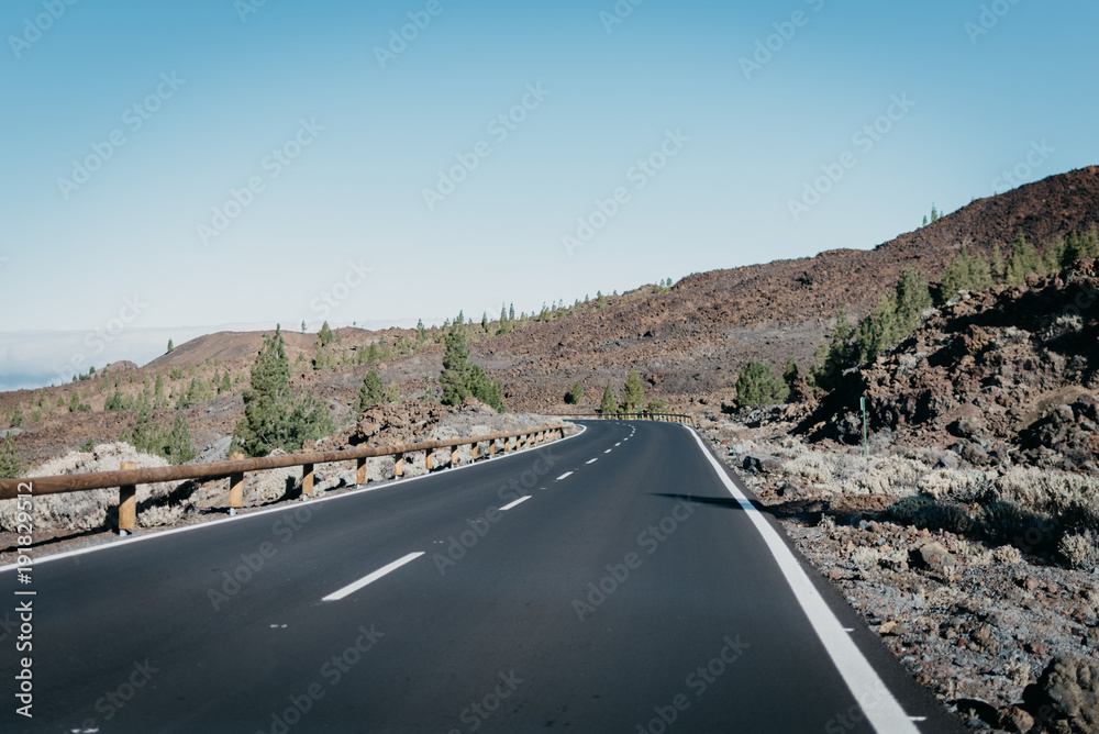 Highway goes through the rocks with green pine-trees to the right near the clouds. Teide National Park. Tenerife