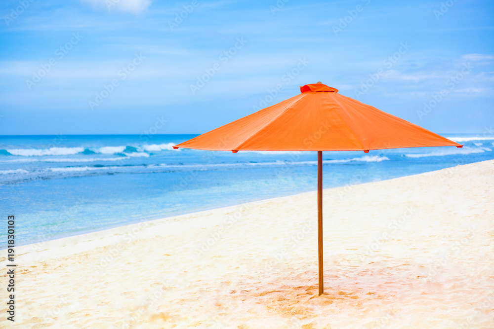 Bright orange parasol on the sand beach. Blue sky and sea in the background