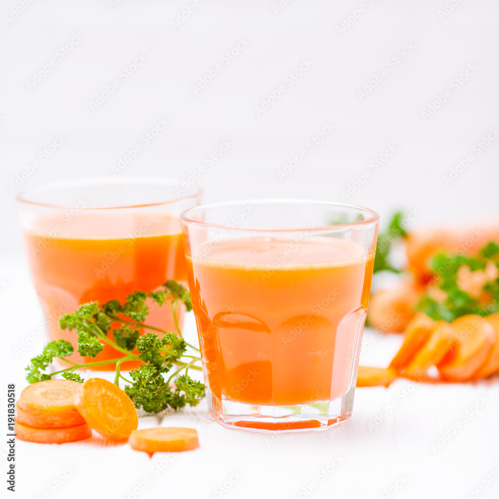 Carrot juice in beautiful glasses, cut orange vegetables and green parsley on white wooden background. Fresh orange drink. Close up photography. Selective focus. Horizontal banner Carrot juice in beautiful glasses, cut orange vegetables and green parsley on white wooden background. Fresh orange drink. Close up photography. Selective focus. Horizontal banner