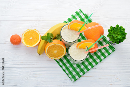 Smoothies with bananas and oranges, a sprig of mint on a white background. Space for text or design.