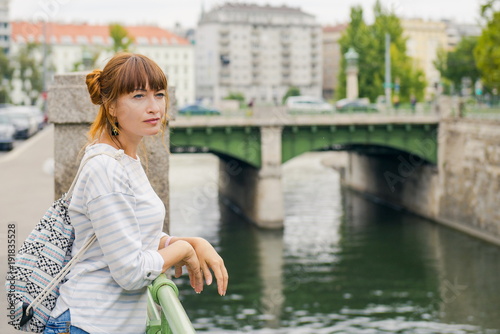 girl tourist walking around the city. Free travel. The girl near the water channel. young woman with a fun hairstyle travels alone with a backpack. Guided tour of Vienna
