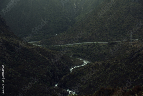 Paisaje montañoso en un día gris y oscuro con un río y una carretera atravesando la imagen