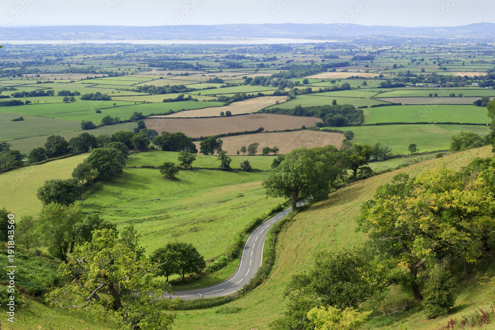 Extensive view towards the River Severn over a patchwork of fields with a winding road in the foreground