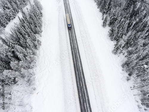 White semitrailer truck fast driving toward on slippery winter asphalt highway, aerial view from drone © Kekyalyaynen