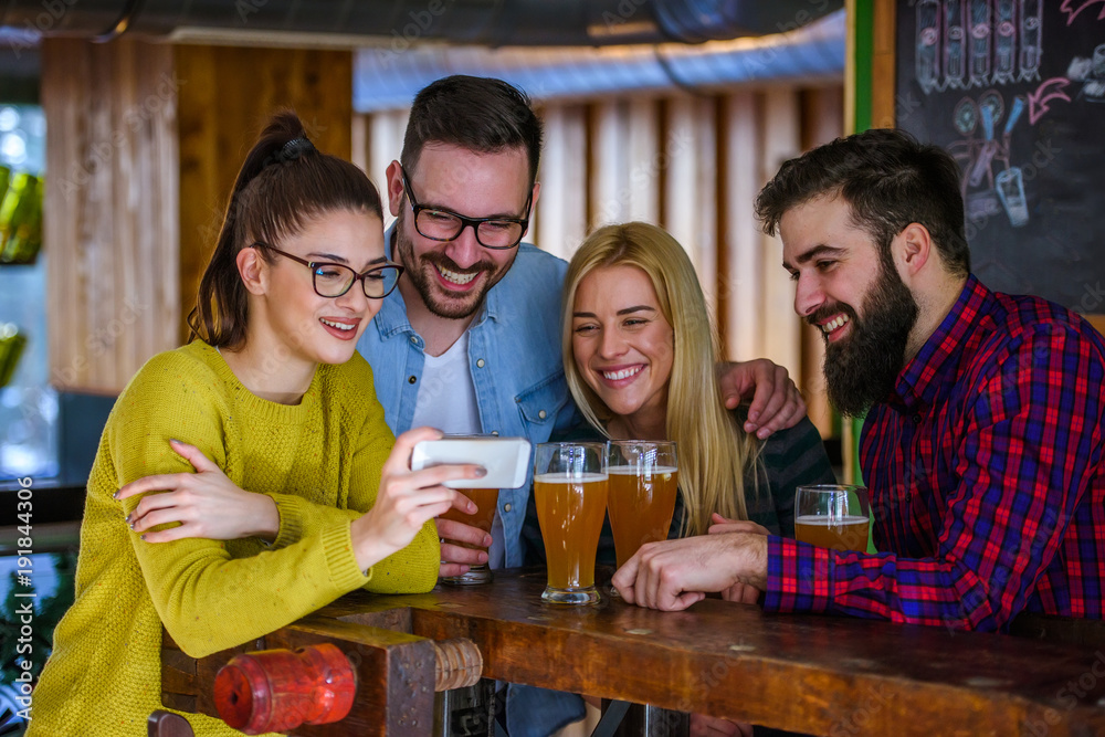Friends in Pub drinking Beer and Looking at Smartphone