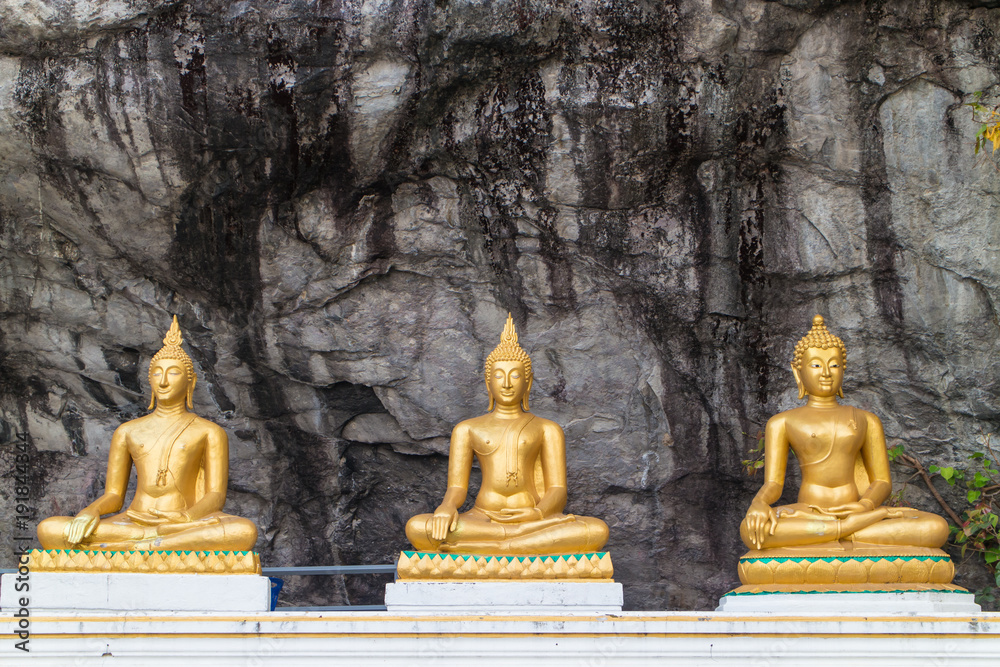 three gold Buddha statue sitting with stone wall background three gold Buddha statue sitting with stone wall background