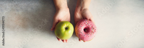 Young woman in white T-shirt choosing between green apple or junk food, donut. Healthy clean detox eating concept. Vegetarian, vegan, raw concept. Copy space. Banner