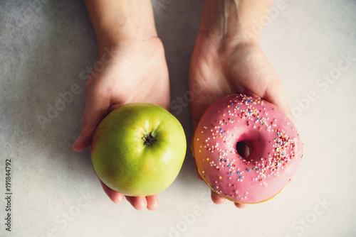 Young woman in white T-shirt choosing between green apple or junk food, donut. Healthy clean detox eating concept. Vegetarian, vegan, raw concept. Copy space