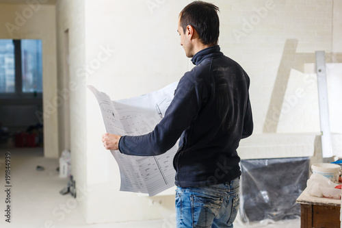 Schilderij op canvas Handsome repairman or builder working with drawings on renovation of apartment i