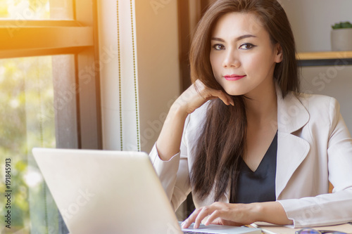 startup business in Asia concept. focused young Asian business woman with thinking face working with laptop at workplace looking at camera, film effect and sun flare effect. © asiandelight