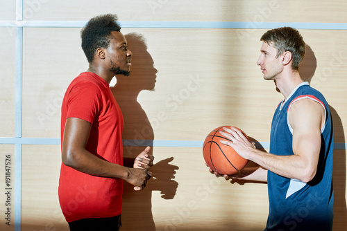 Serious handsome young interracial friends talking about basketball while discussing plan of game and thinking of technique in gym