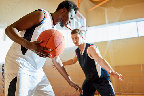 Fotografie Concentrated sporty young African-American basketball player moving with ball on