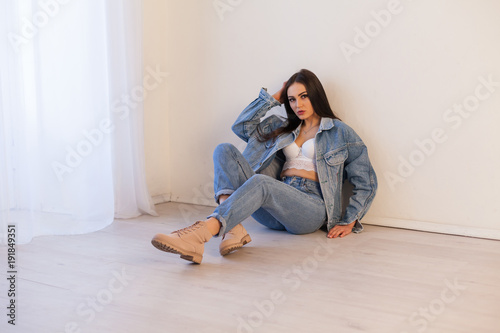 beautiful girl in jeans clothes sitting on the floor in a white room