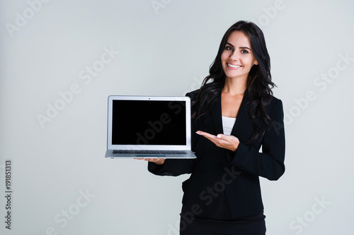 Have you seen this program? Beautiful young businesswoman showing her laptop and looking at camera with smile while standing against white background
