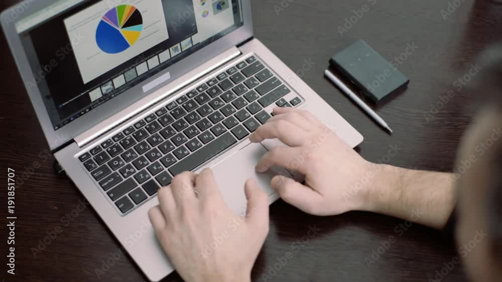 Person Typing on a modern laptop in an office. the man is looking at the graph on the laptop. Person Typing on a modern laptop in an office. the man is looking at the graph on the laptop.
