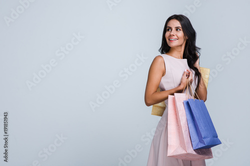 In love with shopping. Beautiful young woman holding shopping bags and looking away with smile while standing against white background