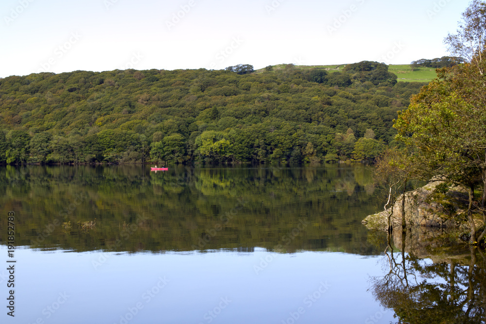 A canoe passes by on Coniston Water on a dead calm early autumn morning in the Lake District, Cumbria, UK
