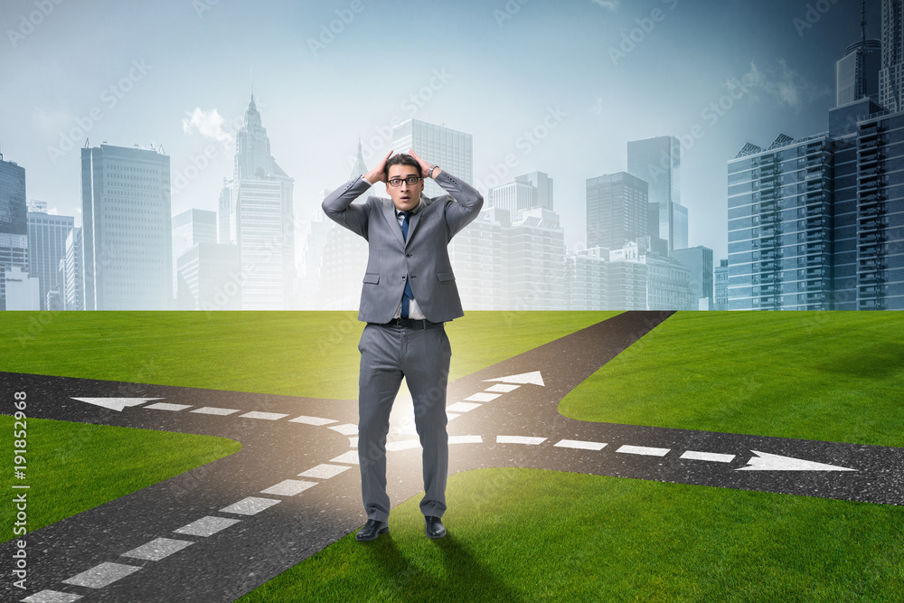 Young businessman at crossroads in uncertainty concept Young businessman at crossroads in uncertainty concept