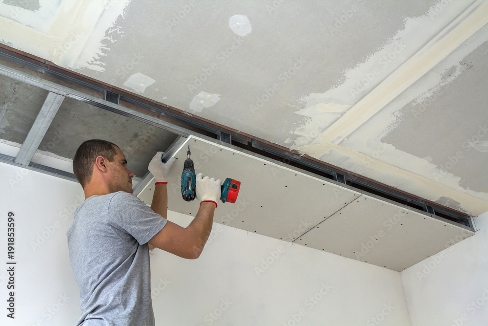 Construction worker assemble a suspended ceiling with drywall and fixing  the drywall to the ceiling metal frame with screwdriver. Photos | Adobe  Stock