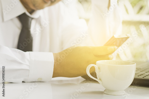 Businessmen who are determined to work, are updating cell phone news in the morning, have coffee and laptop on the table.