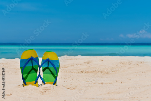 sandal flipflops on a sandy ocean beach with blue sea and blue background