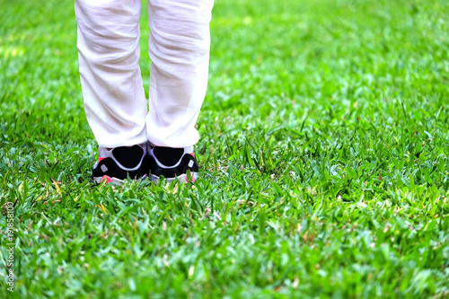 Woman's legs whith white pants and sneaker stand on the green grass field in daylight.