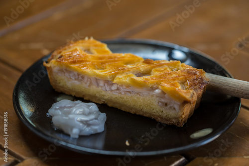 One piece coconut tart large is placed on a black plate. Looks very appetizing, on a wooden table.