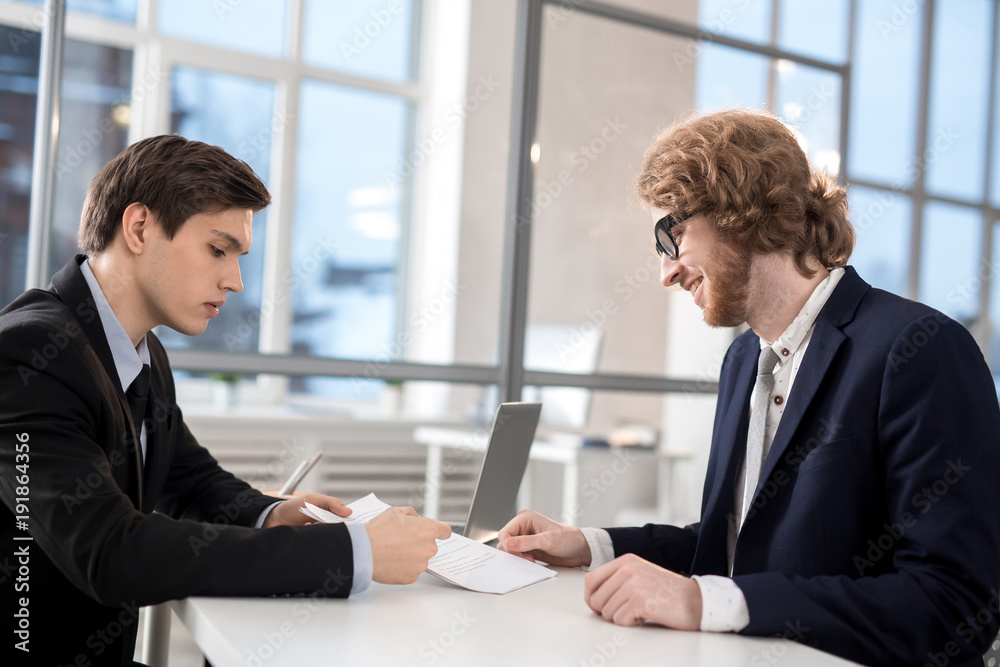 Confident agent pointing at contract while explaining his client where to sign it Confident agent pointing at contract while explaining his client where to sign it