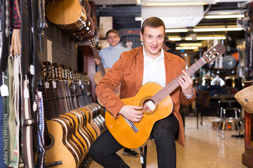 male customer deciding on acoustic guitar in musical shop