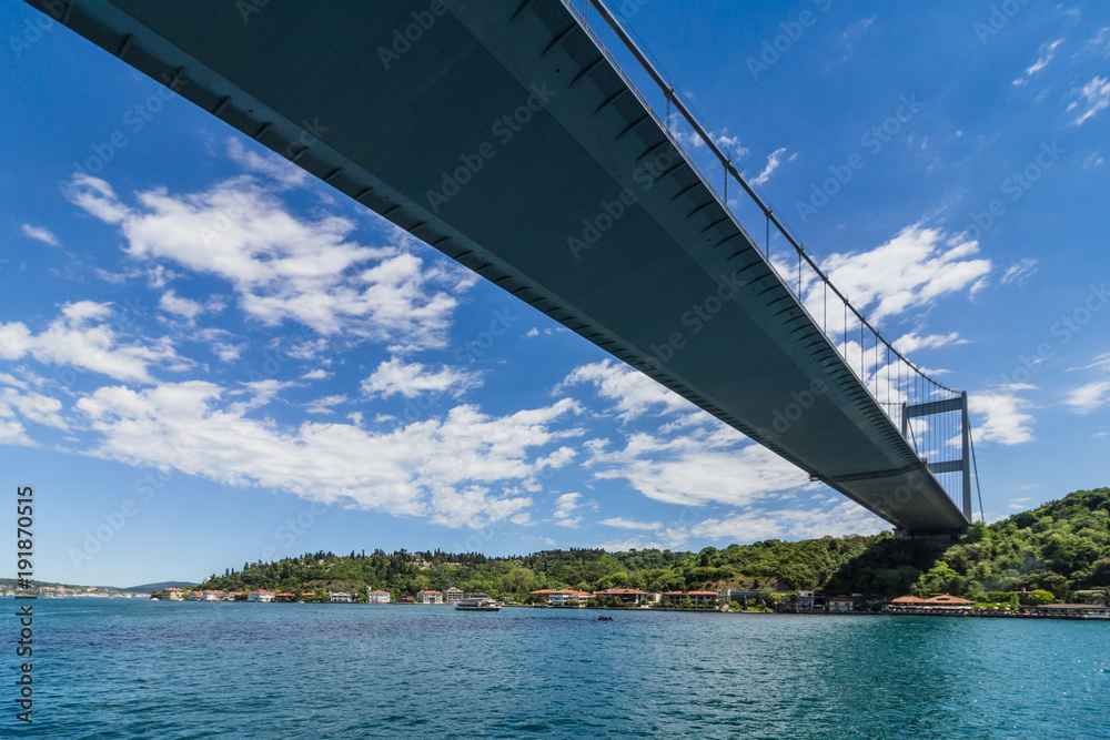 View of Fatih Sultan Mehmet Bridge which is localed on Bosphorus strait . Ships passing through bridge connecting Europe and Asia. Sunny day with background of cloudy blue sky. Istanbul. Turkey.