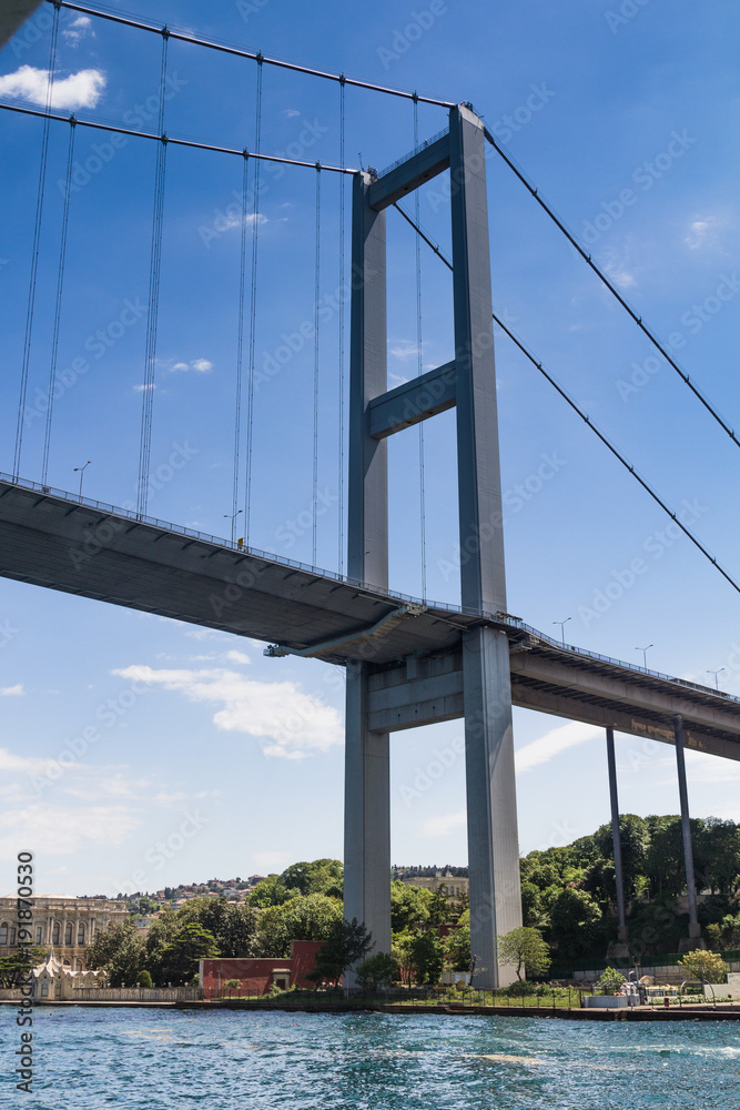 View of the First Bosporus Bridge. Ships passing through bridge connecting Europe and Asia. Sunny day with background of cloudy blue sky. Istanbul. Turkey. View of the First Bosporus Bridge. Ships passing through bridge connecting Europe and Asia. Sunny day with background of cloudy blue sky. Istanbul. Turkey.