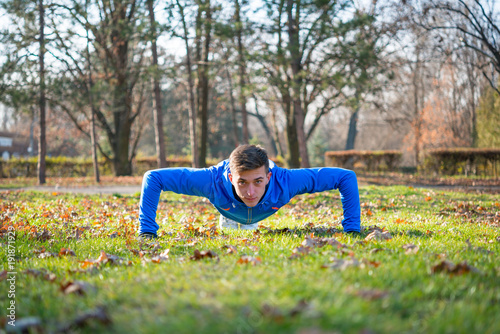 Male Runner Doing Push Up on the Green Lawn in the Park in Sunny Autumn Morning. Healthy Lifestyle and Sport Concept.