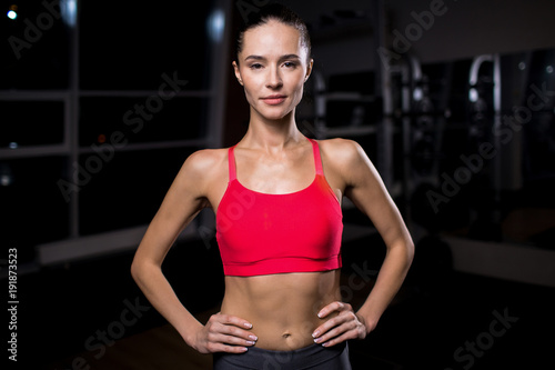 Fit female in akimbo pose looking at camera in sports club