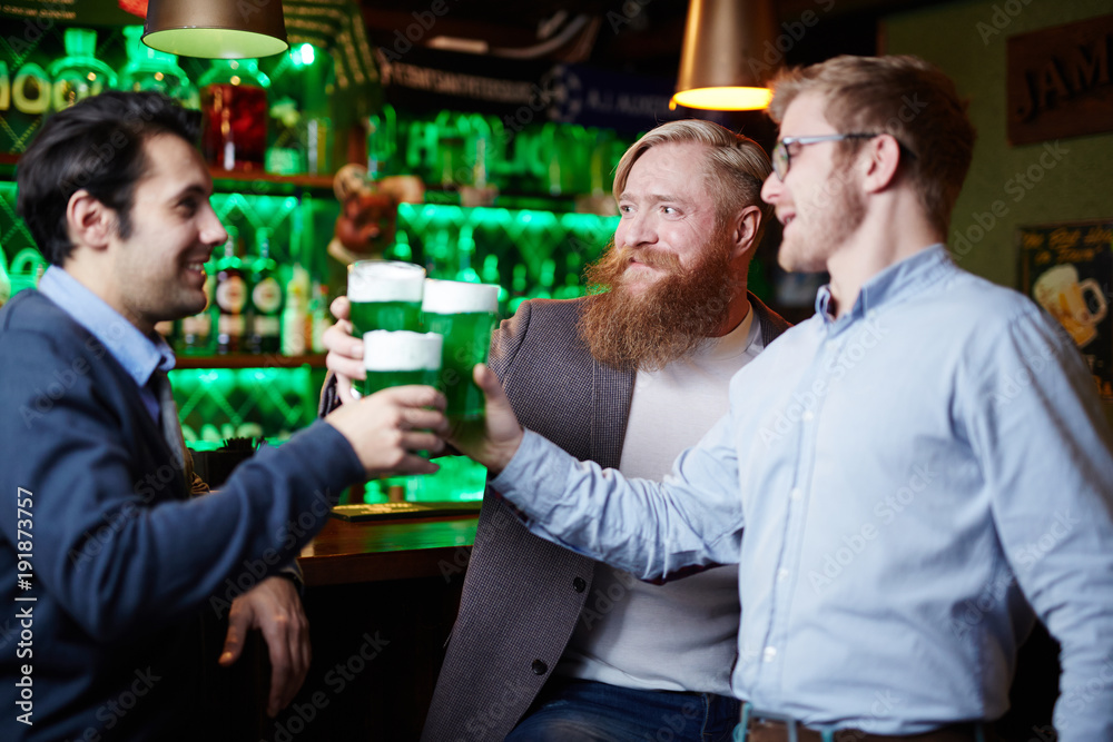 Group of friendly men toasting with green foaming beer while spending time in pub