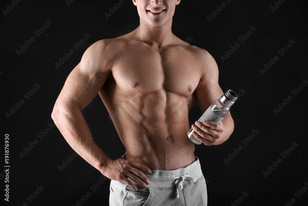 Handsome muscular young man with bottle of water on black background