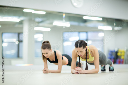 Two friendly girls making effort while doing planks during workout in gym