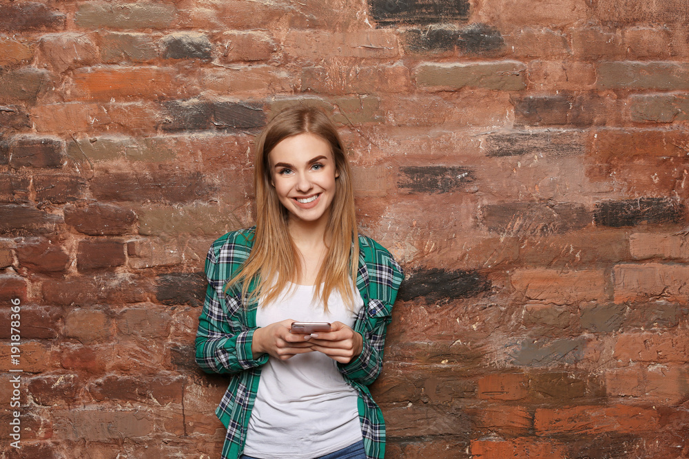 Beautiful young woman with mobile phone near brick wall